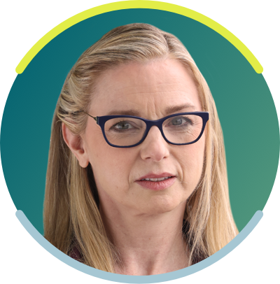 A white woman with long blonde hair and dark glasses faces the camera with a neutral smile.
